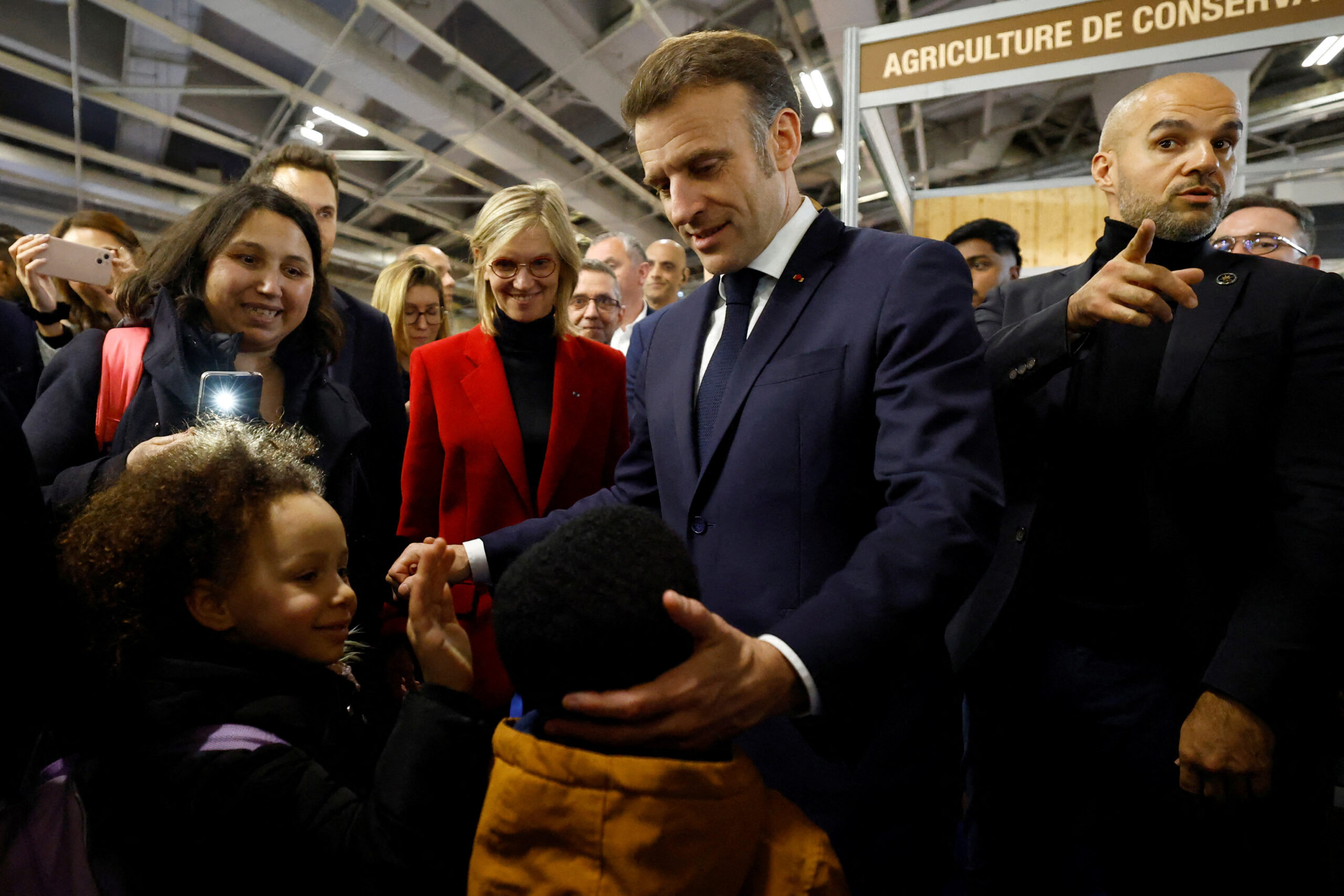 France's President Emmanuel Macron (C) interacts with young attendees during the opening day and inauguration of the 61st International Agricultural Fair (Salon de l'Agriculture) at the Porte de Versailles exhibition centre in Paris on February 22, 2025. The 2025 edition of the SIA (Salon International de l'Agriculture) Agriculture is held in Paris from February 22, to March 2, 2025. (Photo by Sarah Meyssonnier / POOL / AFP)